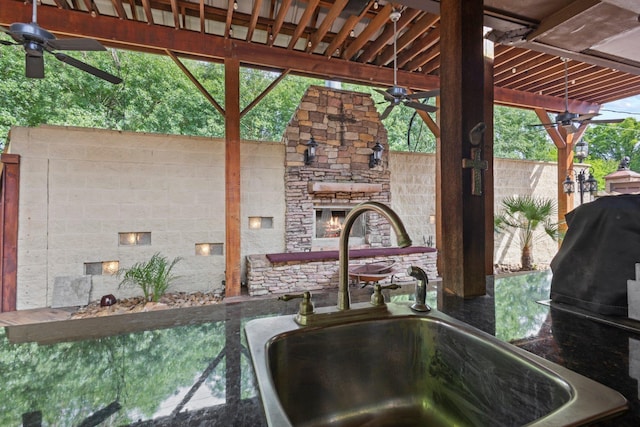 kitchen view of an outdoor stone fireplace, a sink, and a ceiling fan