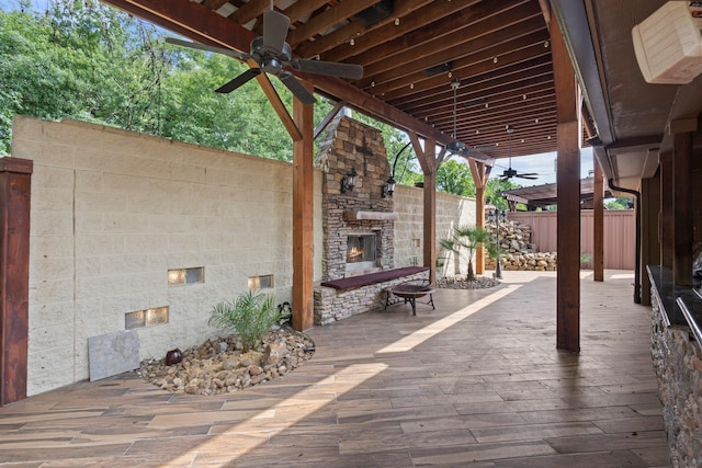 view of patio / terrace featuring an outdoor stone fireplace, a ceiling fan, fence, and a wooden deck