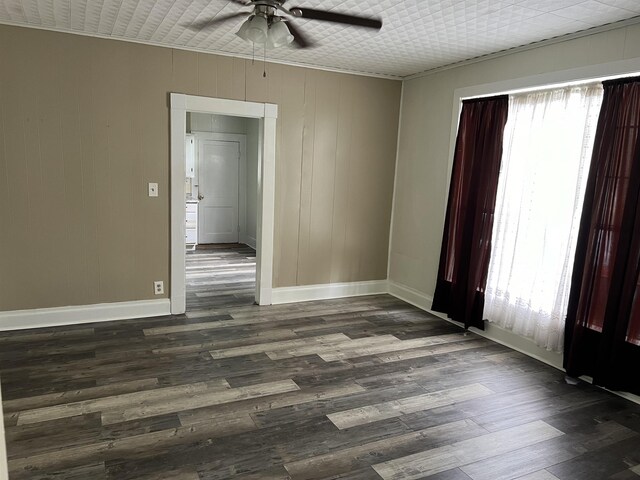 empty room with ceiling fan, crown molding, and dark wood-type flooring