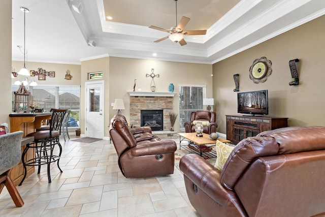 tiled living room featuring a tray ceiling, a stone fireplace, ceiling fan, and ornamental molding