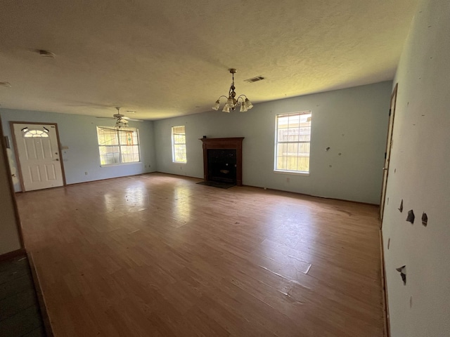 unfurnished living room with a chandelier, wood finished floors, a textured ceiling, and a fireplace with flush hearth