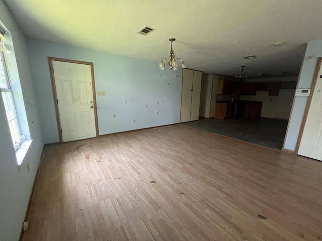 unfurnished living room with a chandelier, wood finished floors, and baseboards