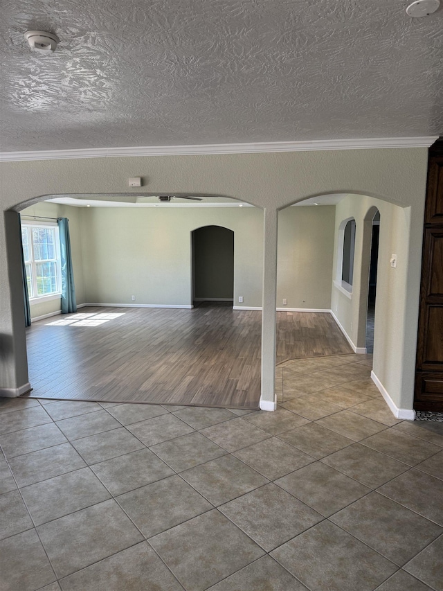 tiled spare room featuring crown molding, arched walkways, and a textured ceiling