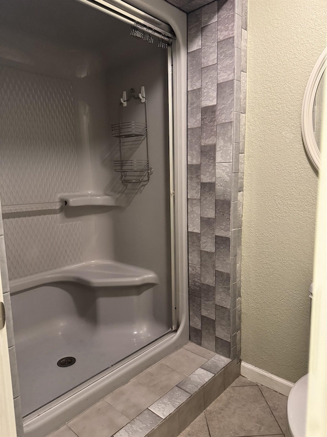 full bath with tile patterned floors, a shower stall, baseboards, and a textured wall