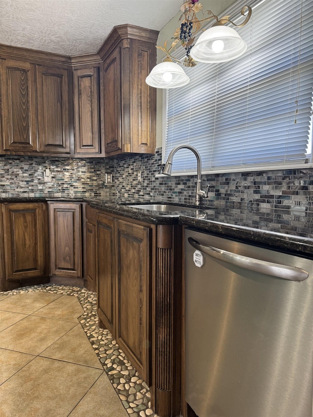 kitchen featuring tasteful backsplash, dishwasher, light tile patterned floors, dark stone countertops, and a sink