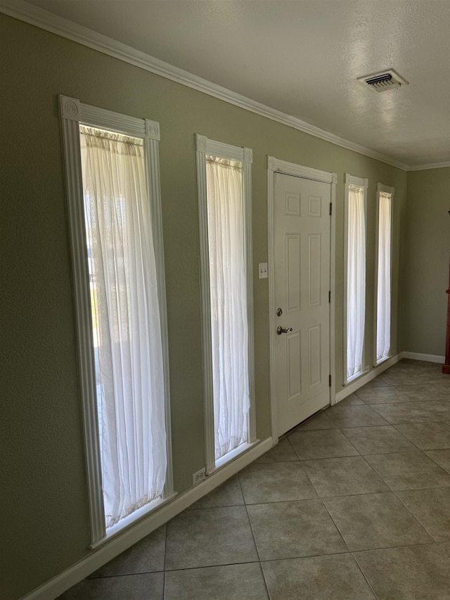 tiled foyer entrance with visible vents, crown molding, and baseboards