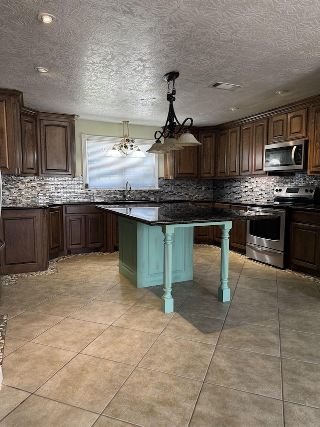 kitchen featuring visible vents, light tile patterned floors, decorative backsplash, appliances with stainless steel finishes, and a kitchen breakfast bar