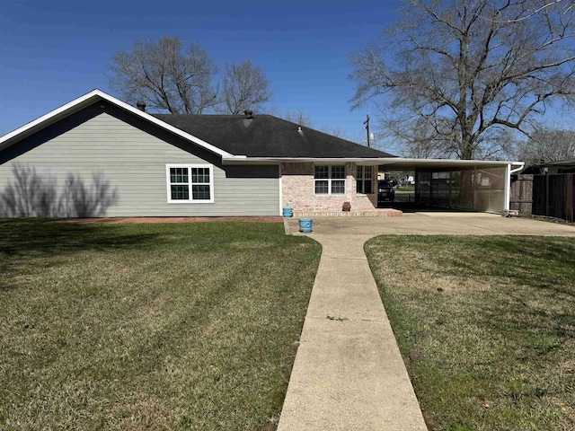 rear view of property with brick siding, a carport, a lawn, and fence