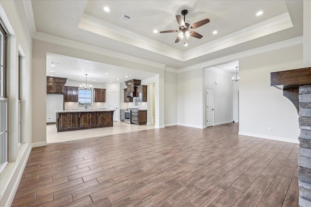 unfurnished living room with sink, crown molding, hardwood / wood-style flooring, ceiling fan with notable chandelier, and a raised ceiling