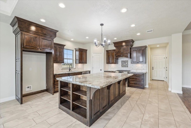 kitchen featuring pendant lighting, sink, dark brown cabinets, a center island, and light stone countertops