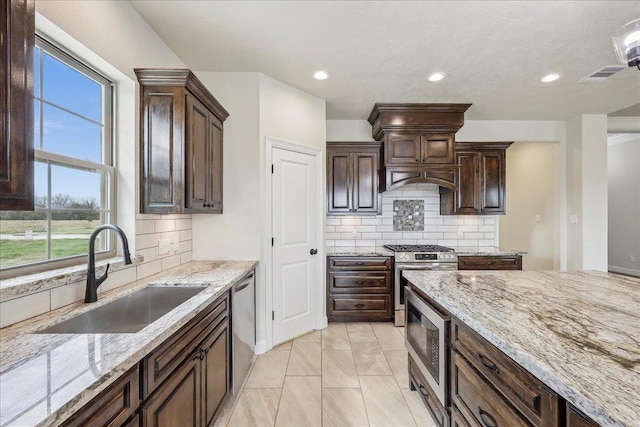 kitchen with stainless steel appliances, light stone countertops, sink, and dark brown cabinets