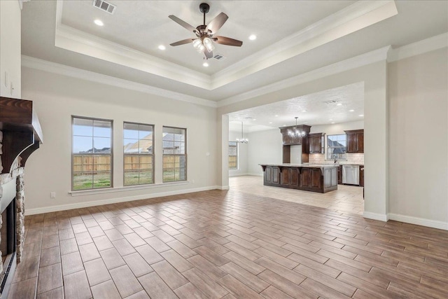 unfurnished living room featuring a tray ceiling, light hardwood / wood-style flooring, ornamental molding, and ceiling fan with notable chandelier