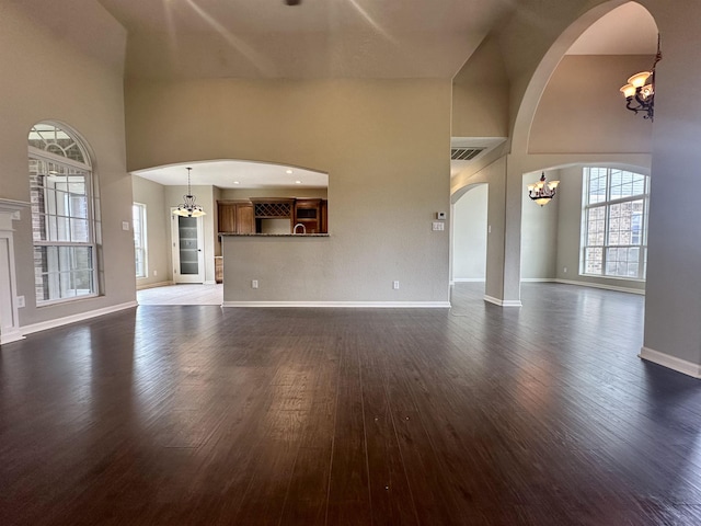 305 Tyler Dr, Bridge City, TX 77630 - unfurnished living room with a chandelier, a high ceiling, arched walkways, dark wood-style floors, and baseboards