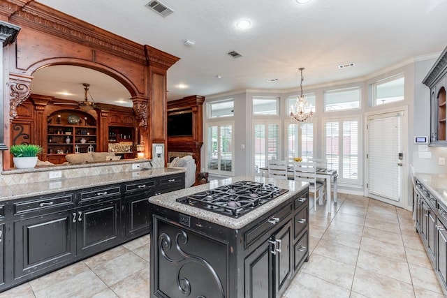 kitchen with light stone countertops, a center island, hanging light fixtures, an inviting chandelier, and gas stovetop