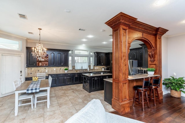 kitchen with stainless steel appliances, an inviting chandelier, kitchen peninsula, crown molding, and decorative backsplash