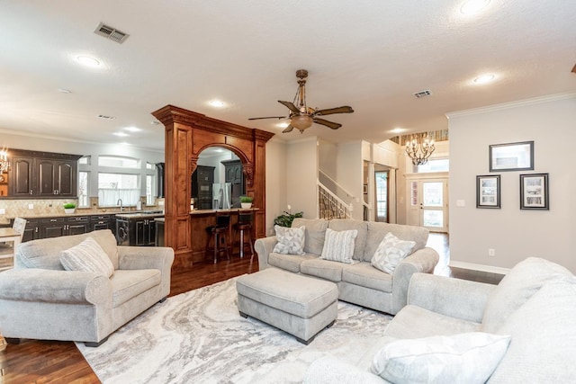 living room featuring a wealth of natural light, crown molding, ceiling fan with notable chandelier, and light wood-type flooring