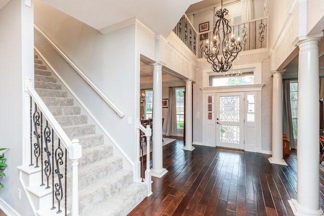 entryway featuring dark wood-type flooring, a high ceiling, an inviting chandelier, decorative columns, and crown molding