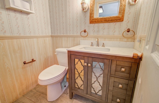 bathroom with a wainscoted wall, toilet, vanity, and wallpapered walls