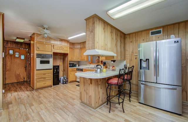 kitchen featuring light countertops, light wood-style flooring, range hood, a peninsula, and white appliances