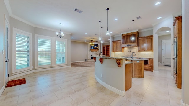 kitchen with a breakfast bar area, light stone counters, tasteful backsplash, an island with sink, and decorative light fixtures