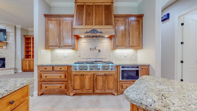 kitchen with premium range hood, a stone fireplace, light stone counters, ornamental molding, and appliances with stainless steel finishes