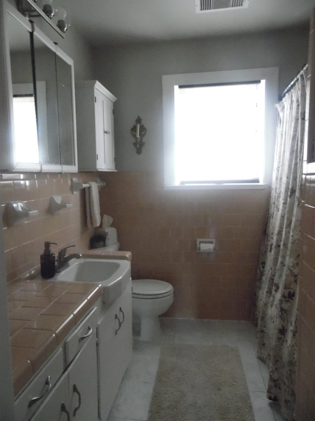 full bath with toilet, a shower with shower curtain, visible vents, vanity, and tile walls