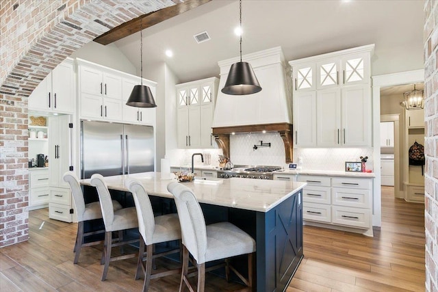 kitchen featuring tasteful backsplash, custom range hood, a kitchen island with sink, sink, and white cabinetry