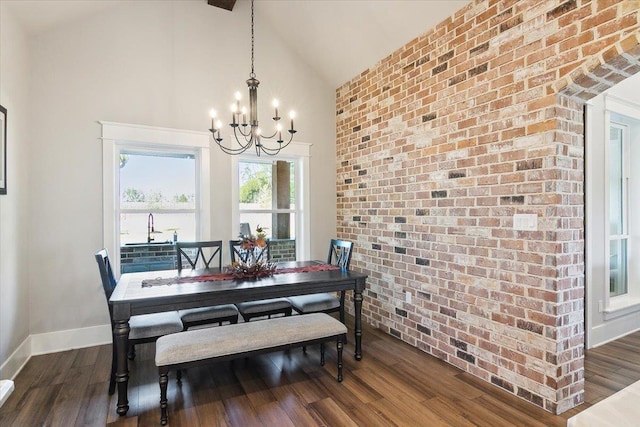 dining room featuring high vaulted ceiling, dark wood-type flooring, brick wall, and a chandelier