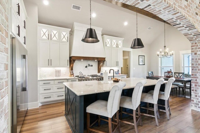 kitchen featuring hanging light fixtures, high end refrigerator, premium range hood, backsplash, and a center island with sink