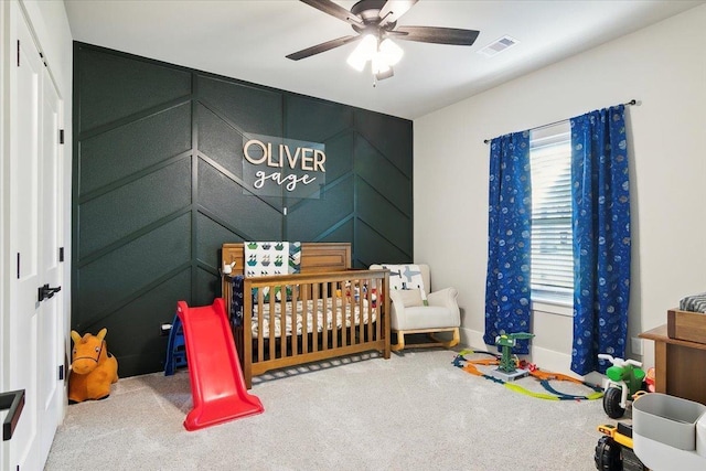 carpeted bedroom featuring ceiling fan and a nursery area