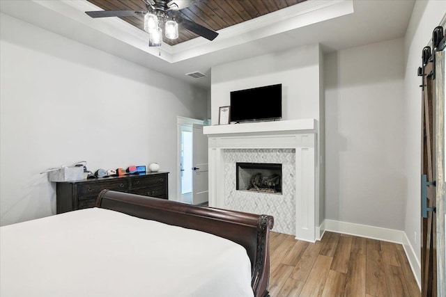 bedroom with a tray ceiling, ceiling fan, crown molding, a tile fireplace, and wood-type flooring