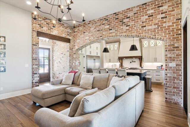 living room with dark hardwood / wood-style flooring, a notable chandelier, and brick wall