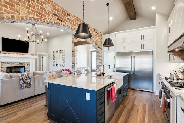 kitchen with pendant lighting, an island with sink, beamed ceiling, premium appliances, and white cabinetry