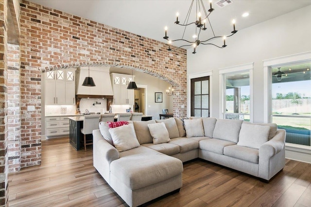 living room with a notable chandelier, wood-type flooring, and brick wall