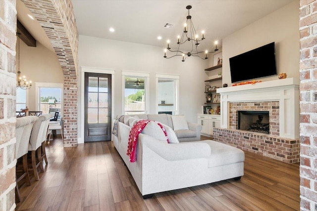 living room with ceiling fan with notable chandelier, dark hardwood / wood-style flooring, a towering ceiling, and a brick fireplace