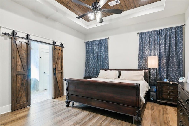 bedroom featuring a raised ceiling, light hardwood / wood-style flooring, ceiling fan, a barn door, and wood ceiling