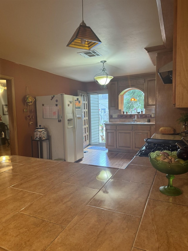 kitchen featuring tasteful backsplash, tile patterned floors, exhaust hood, white refrigerator with ice dispenser, and pendant lighting