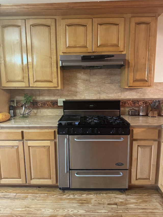 kitchen with tasteful backsplash, tile counters, stainless steel gas range oven, and light hardwood / wood-style flooring