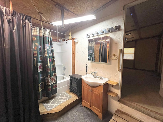 full bath with shower / bath combo, a textured wall, a wood stove, a textured ceiling, and vanity