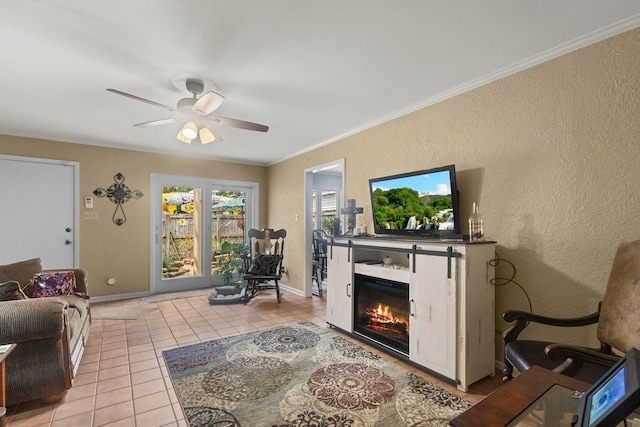 living area featuring light tile patterned floors, ornamental molding, a glass covered fireplace, and ceiling fan