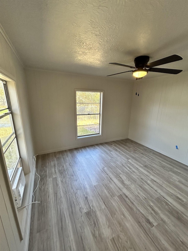 empty room with ceiling fan, a wealth of natural light, a textured ceiling, and light hardwood / wood-style floors