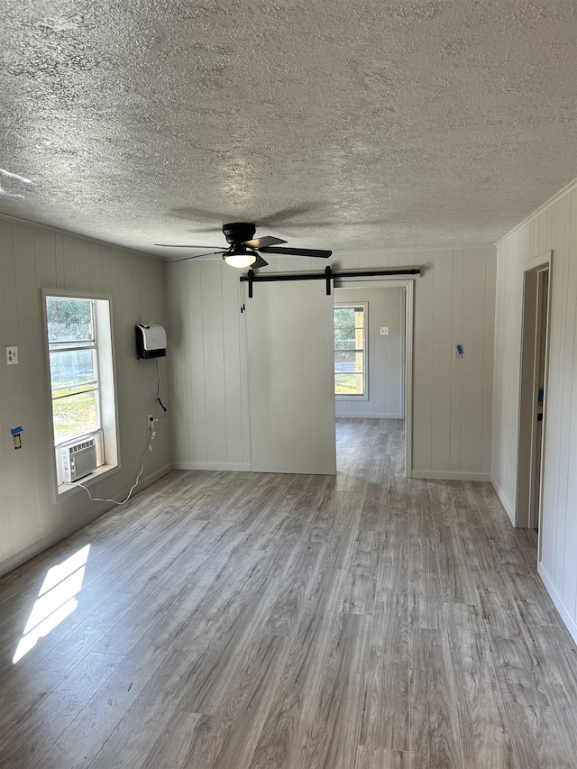 unfurnished room featuring cooling unit, plenty of natural light, a barn door, and light wood-type flooring