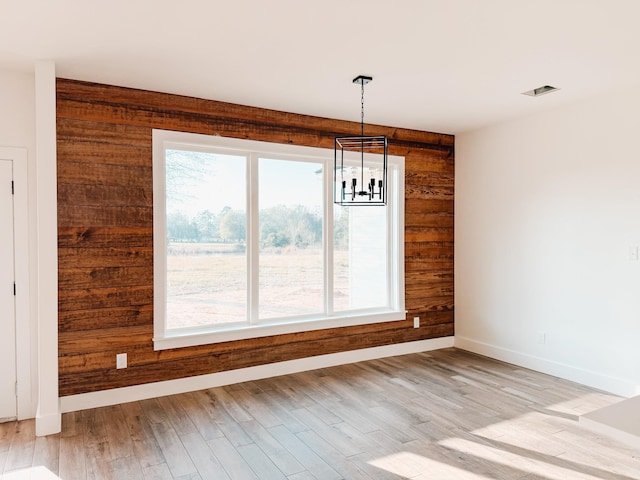 unfurnished dining area with a notable chandelier, wood walls, and light wood-type flooring