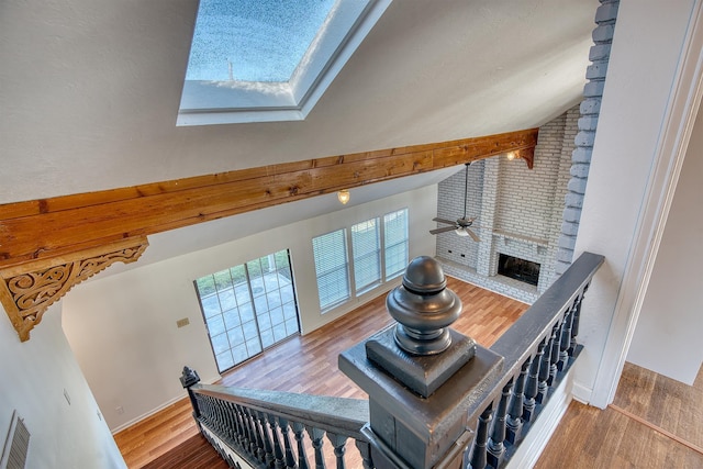 living room with a brick fireplace, vaulted ceiling with skylight, wood-type flooring, and ceiling fan