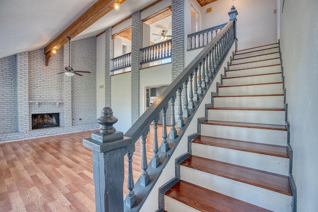 stairway featuring ceiling fan, a fireplace, wood-type flooring, high vaulted ceiling, and beam ceiling