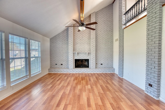 unfurnished living room with ceiling fan, light wood-type flooring, brick wall, a fireplace, and vaulted ceiling