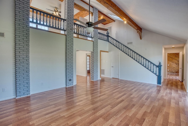 unfurnished living room with high vaulted ceiling, beamed ceiling, and light hardwood / wood-style flooring