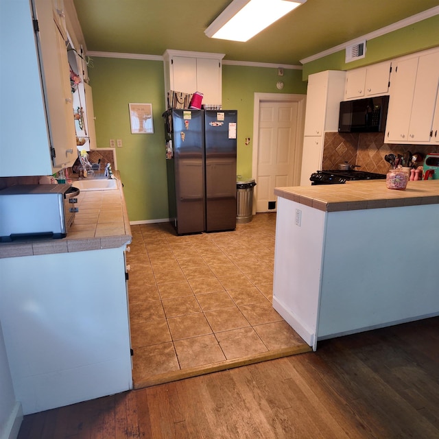 kitchen with tile counters, sink, white cabinets, black appliances, and ornamental molding