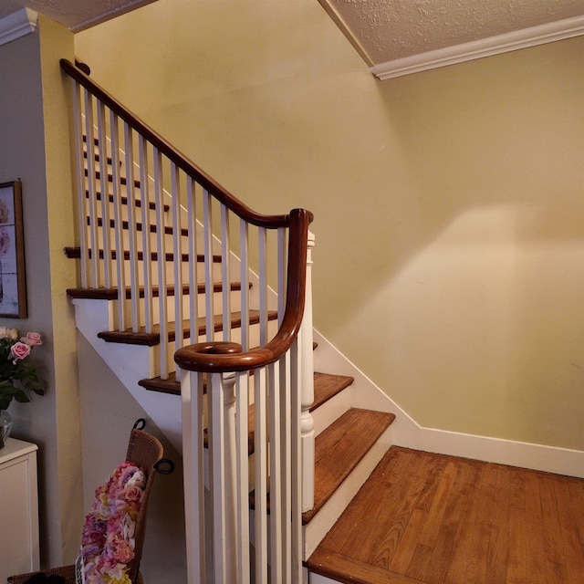 stairs with hardwood / wood-style floors, a textured ceiling, and ornamental molding