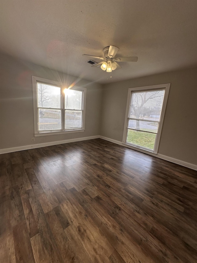 empty room featuring ceiling fan, a healthy amount of sunlight, a textured ceiling, and dark hardwood / wood-style floors